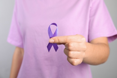 Woman holding purple ribbon on grey background, closeup. Domestic violence awareness