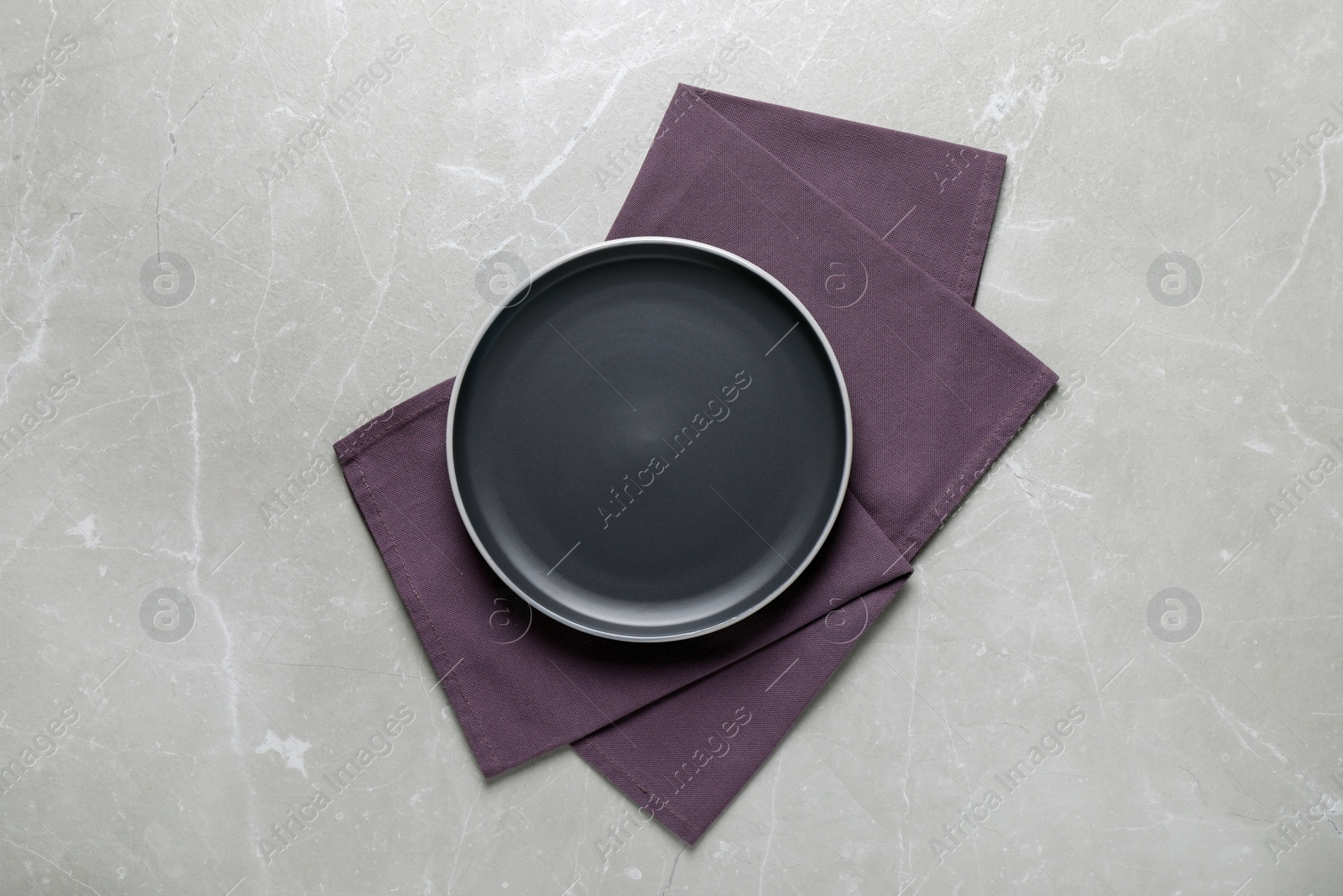 Photo of New dark plate and napkin on light grey table, top view
