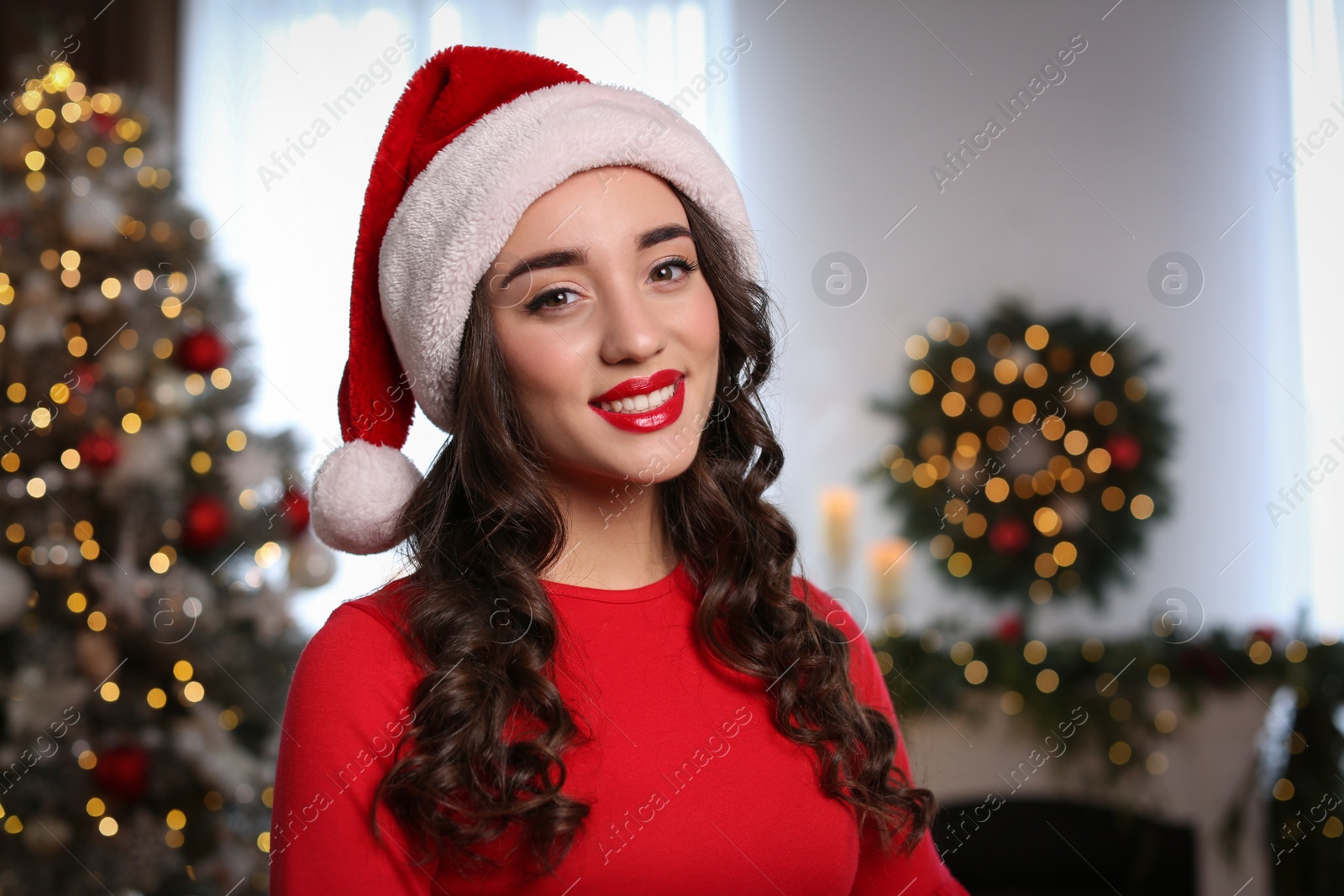 Photo of Beautiful young woman wearing Santa hat in room decorated for Christmas