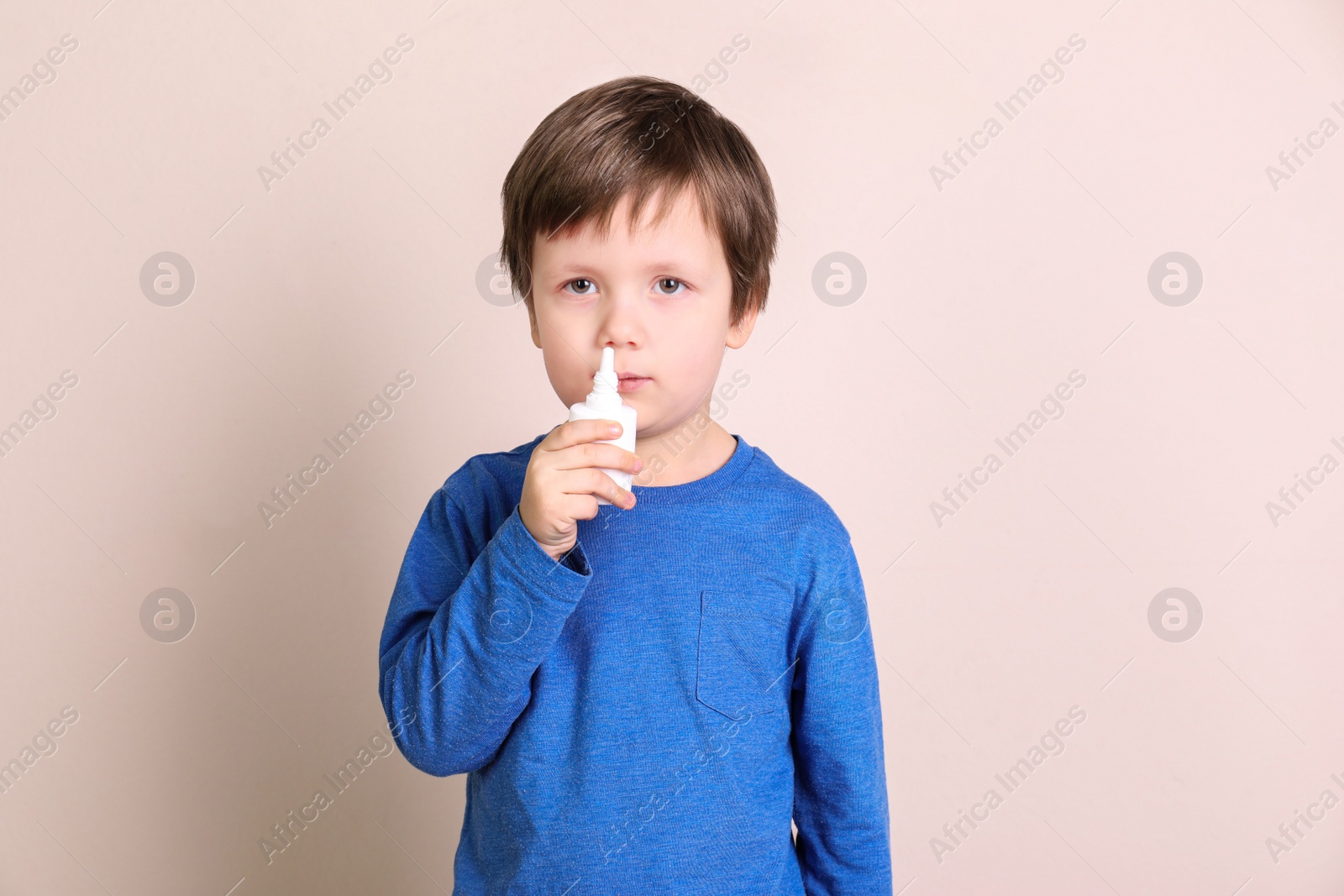 Photo of Sick little boy using nasal spray on light background