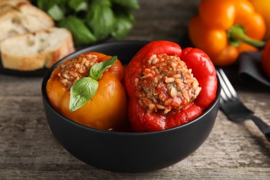 Photo of Delicious stuffed peppers with basil in bowl on wooden table