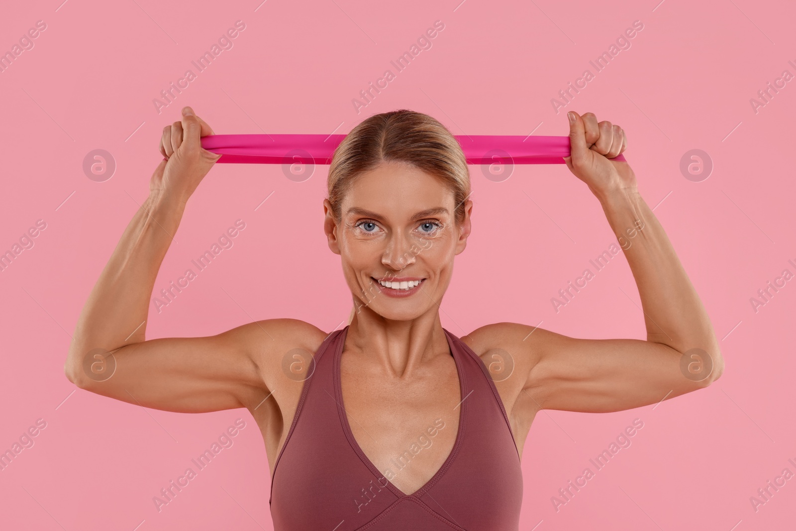 Photo of Woman exercising with elastic resistance band on pink background