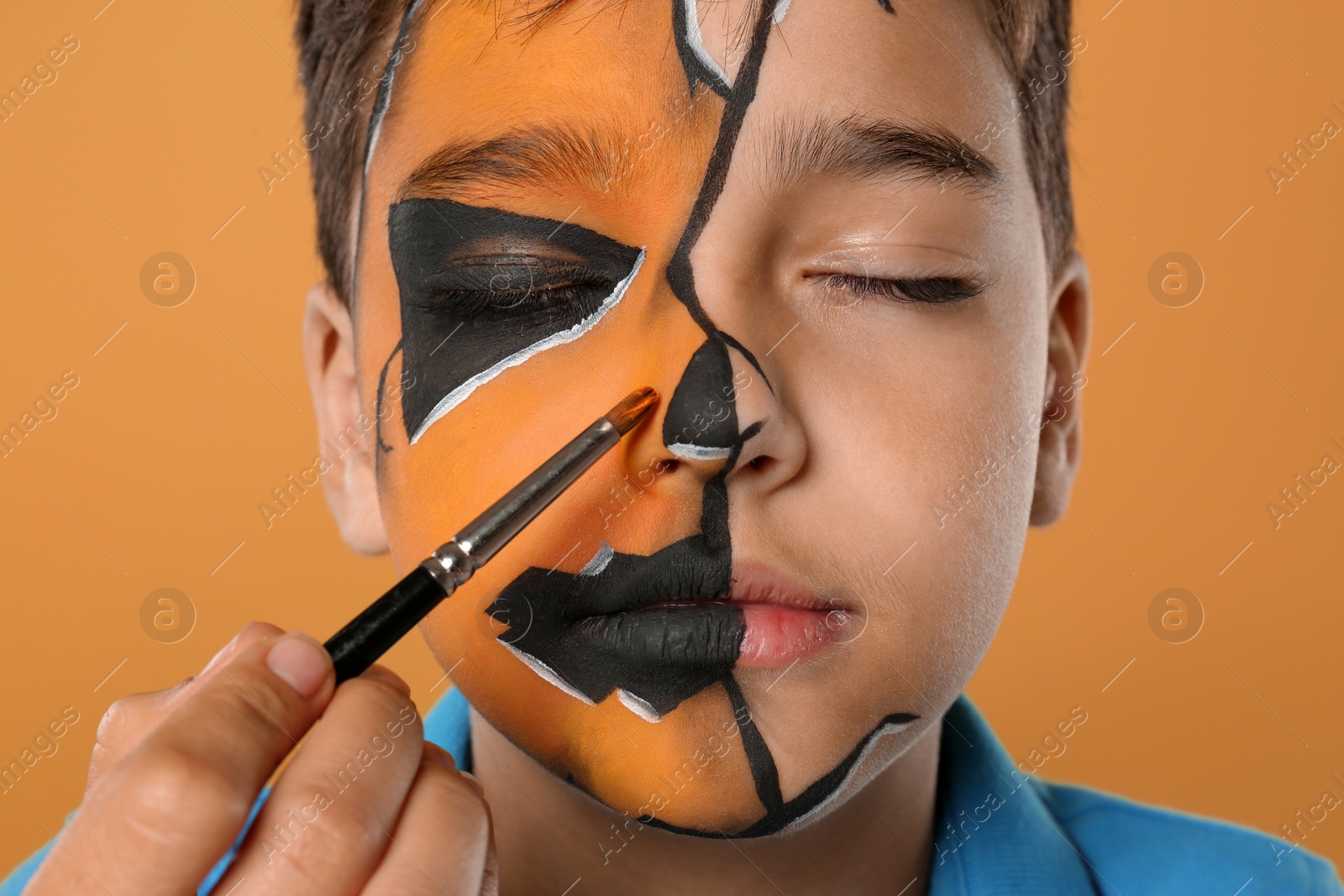 Photo of Artist painting face of little boy on orange background