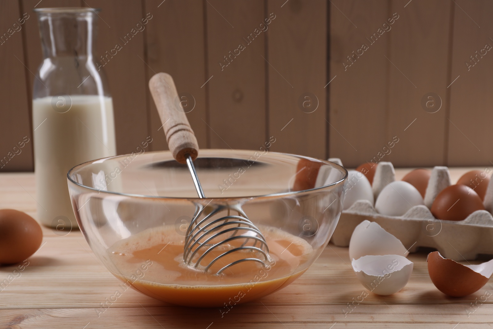 Photo of Making dough. Beaten eggs in bowl, shells and milk on wooden table, closeup