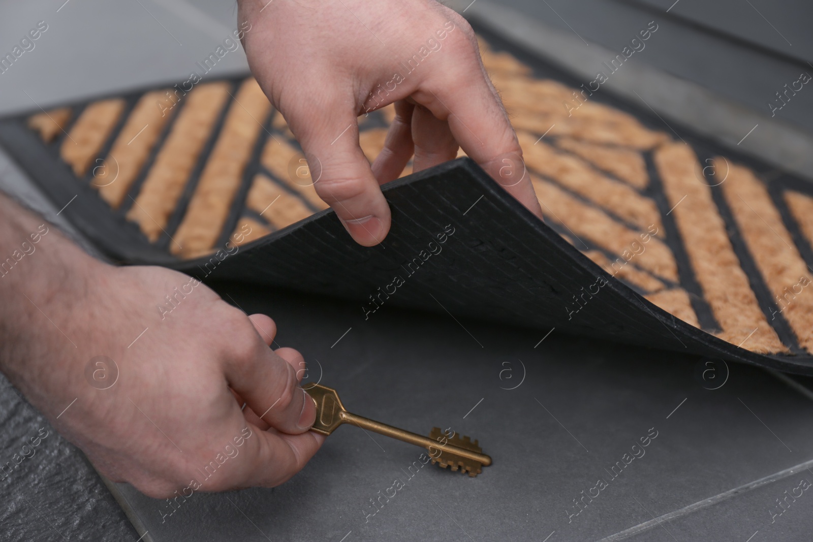 Photo of Man picking up key hidden under door mat, closeup view