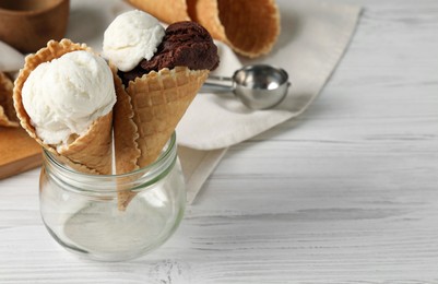 Ice cream scoops in wafer cones on white wooden table, space for text