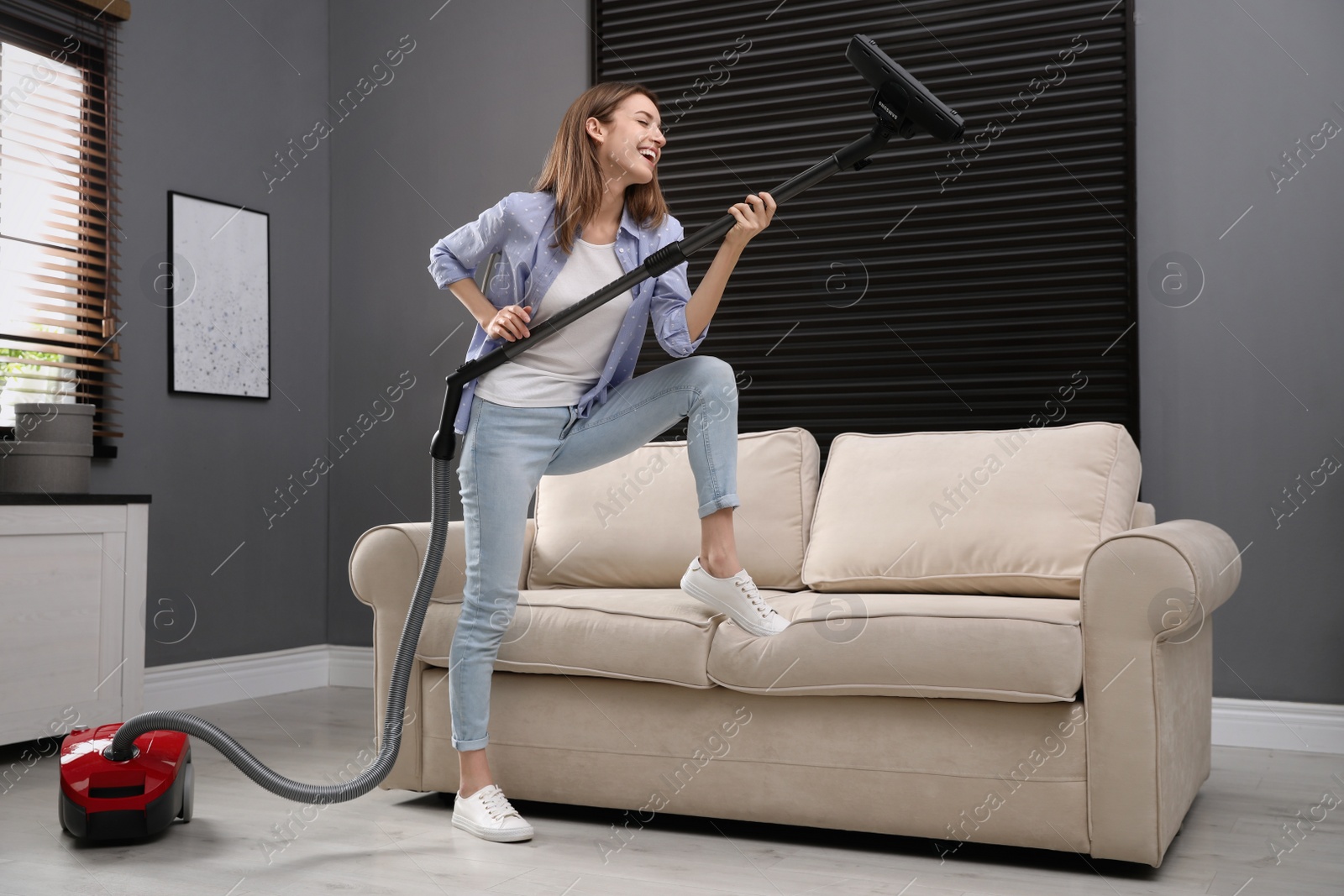 Photo of Young woman having fun while vacuuming at home