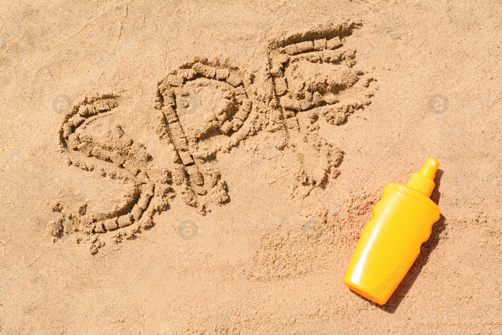 Photo of Abbreviation SPF written on sand and blank bottle of sunscreen at beach, top view