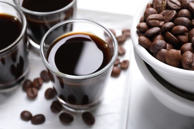 Shot glasses of coffee liqueur and beans on white table, closeup