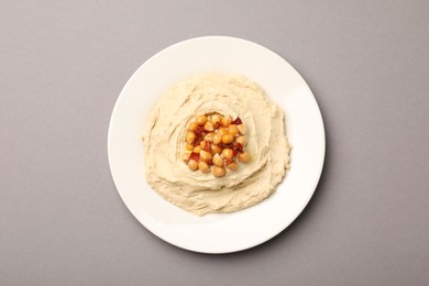Photo of Plate of tasty hummus with chickpeas on grey background, top view