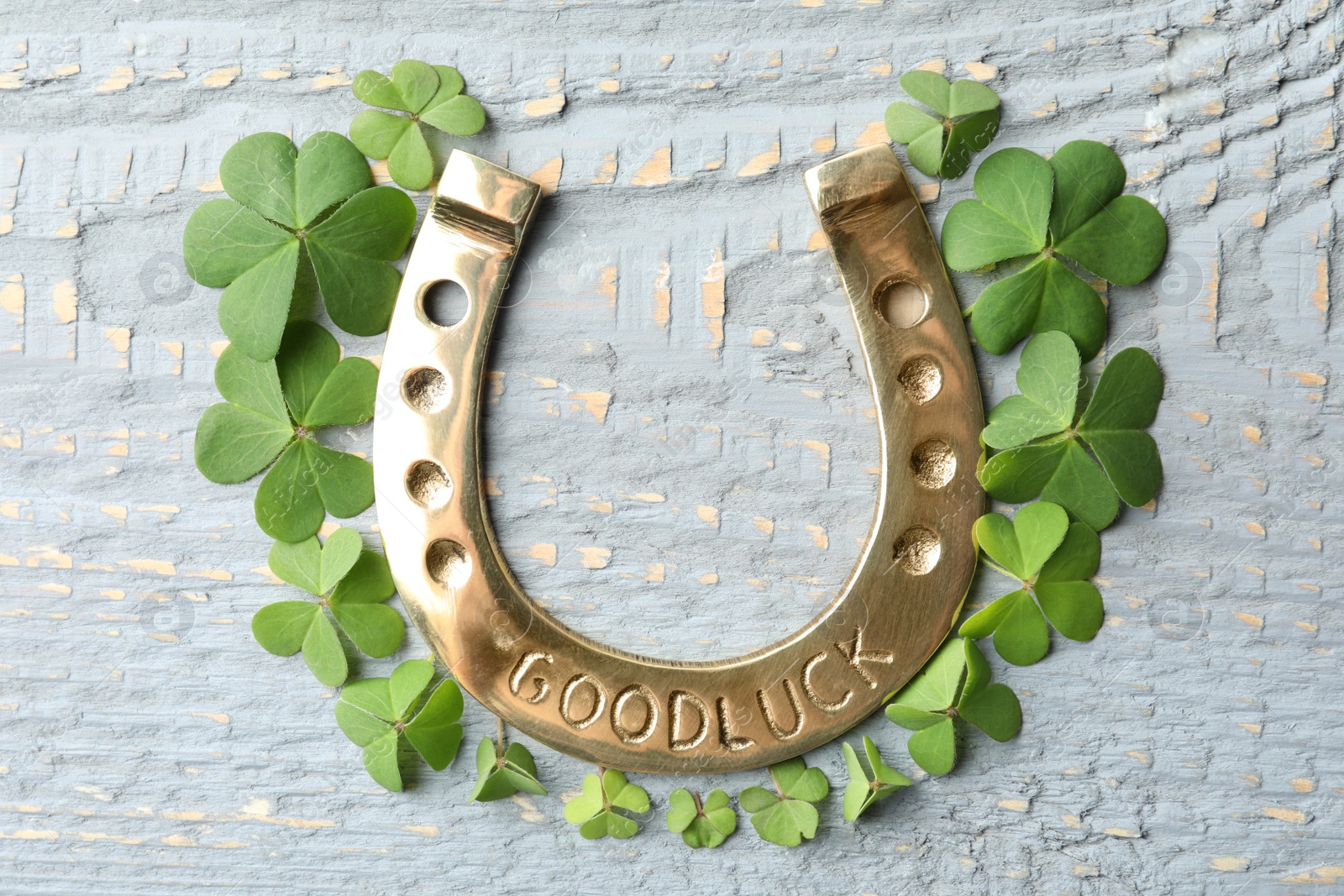 Photo of Clover leaves and horseshoe on wooden table, flat lay. St. Patrick's Day celebration