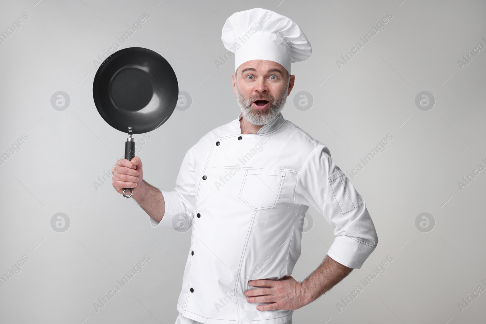 Photo of Surprised chef in uniform holding wok on grey background