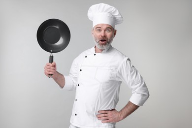 Surprised chef in uniform holding wok on grey background