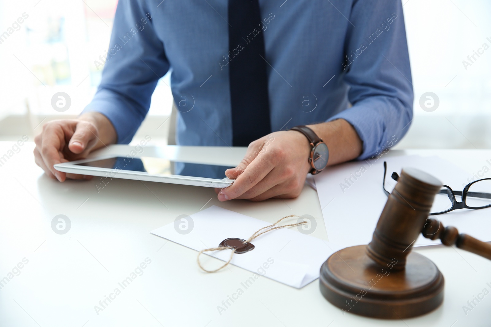 Photo of Notary working with tablet and judge gavel on table, closeup. Law and justice concept