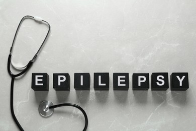 Photo of Black cubes with word Epilepsy and stethoscope on light grey table, flat lay