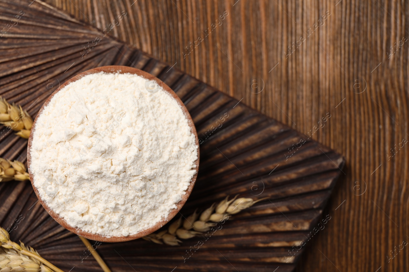 Photo of Bowl of organic wheat flour on wooden table, flat lay. Space for text