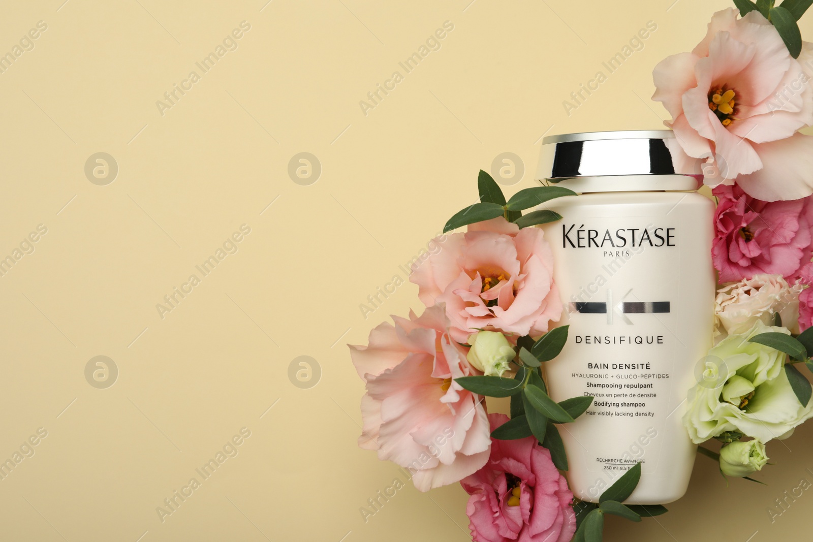 Photo of MYKOLAIV, UKRAINE - SEPTEMBER 07, 2021: Kerastase shampoo and beautiful flowers on beige background, flat lay. Space for text