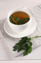 Photo of Aromatic herbal tea and fresh parsley on white wooden table