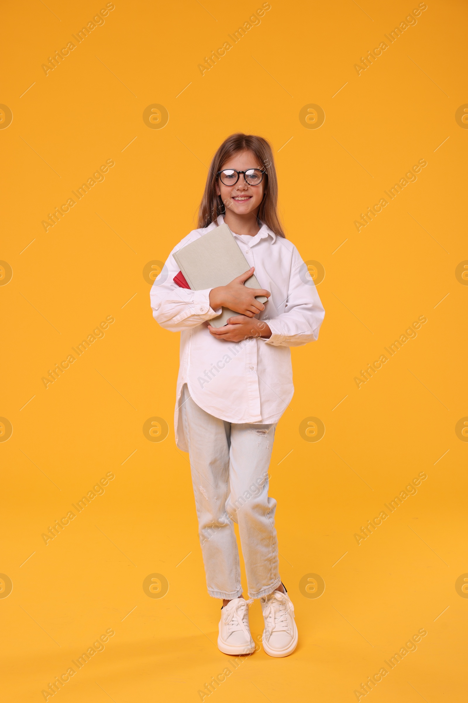 Photo of Happy schoolgirl with books on orange background