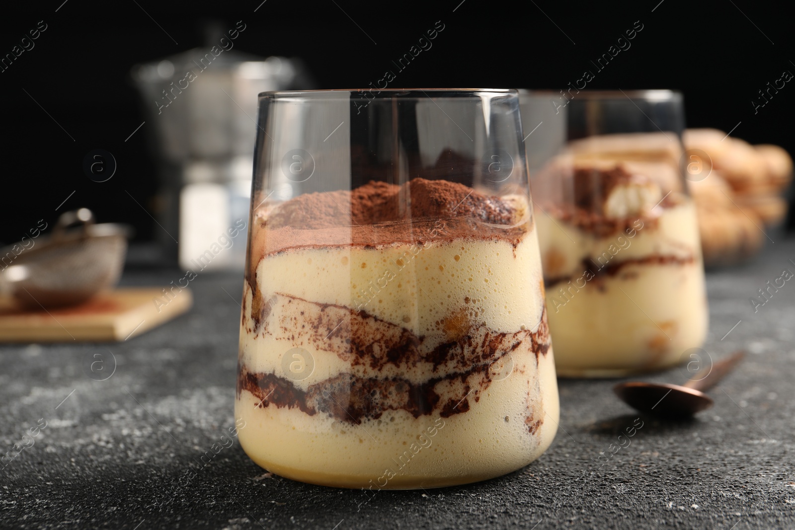 Photo of Delicious tiramisu in glasses on grey textured table, closeup