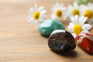 Different gemstones and healing herbs on wooden table, closeup. Space for text