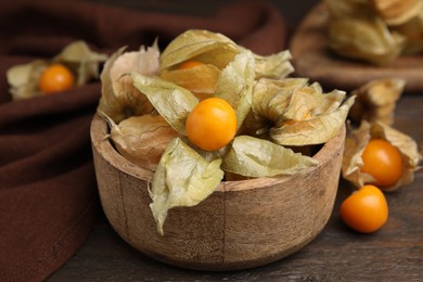 Photo of Ripe physalis fruits with calyxes in bowl on wooden table