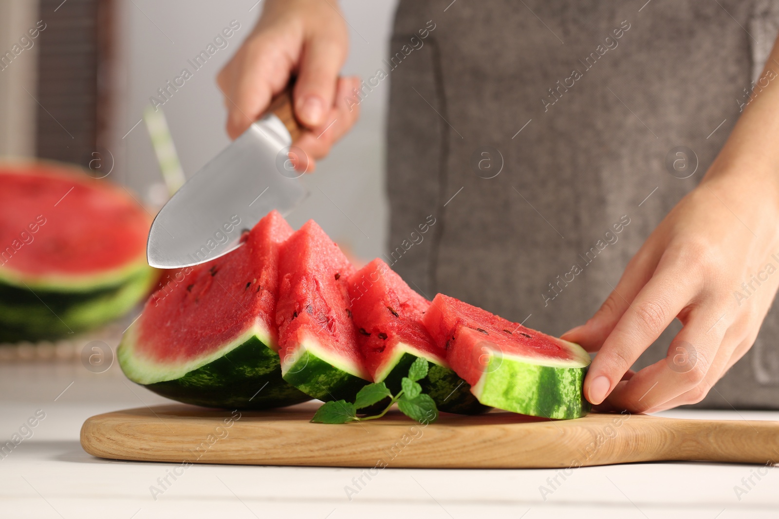 Photo of Woman cutting delicious watermelon at white wooden table indoors, closeup