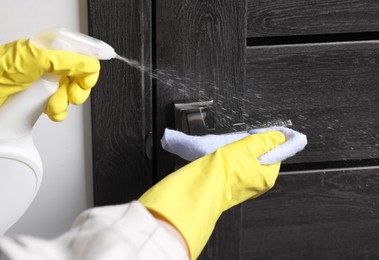 Woman cleaning door handle with detergent and rag indoors, closeup