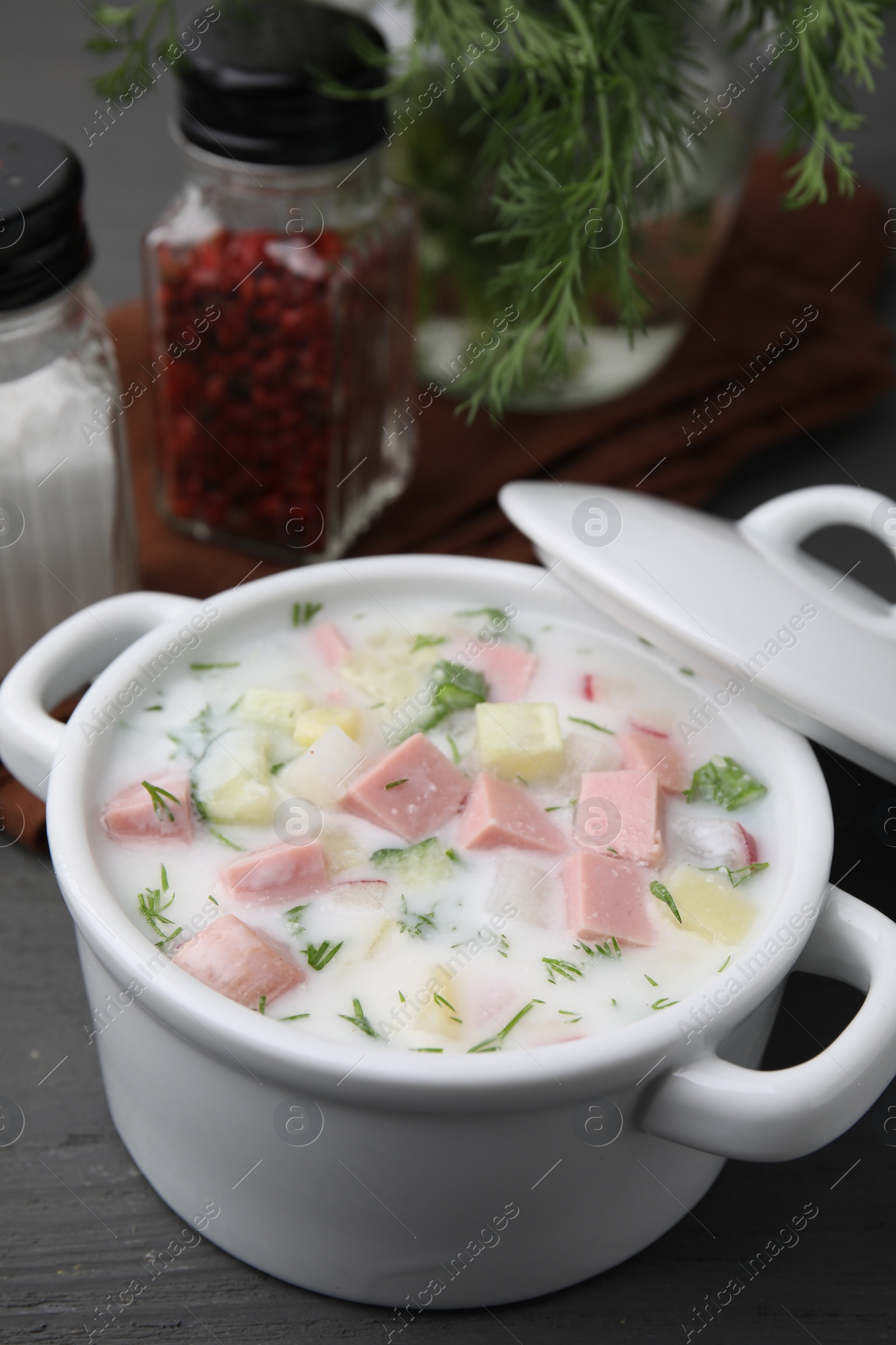 Photo of Delicious cold summer soup (okroshka) with boiled sausage in pot on grey wooden table