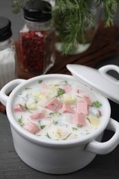 Delicious cold summer soup (okroshka) with boiled sausage in pot on grey wooden table