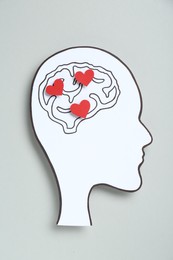 Photo of Emotional thinking. Paper human head cutout with drawing of brain and red hearts on grey background, top view