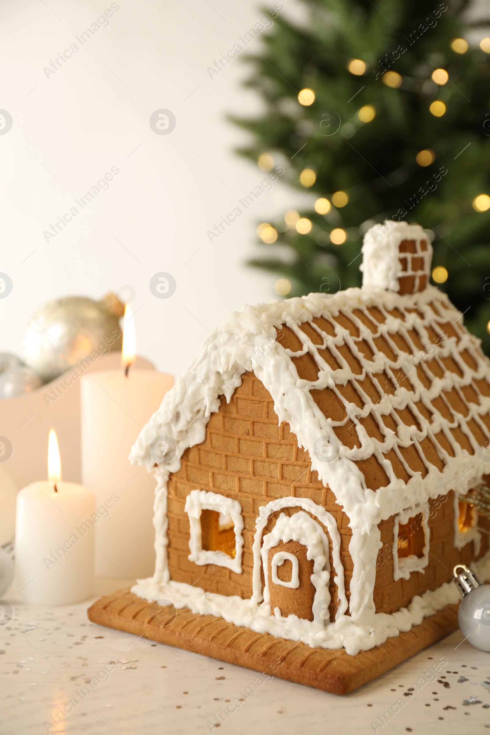 Photo of Beautiful gingerbread house decorated with icing and candles on white table