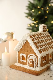 Beautiful gingerbread house decorated with icing and candles on white table