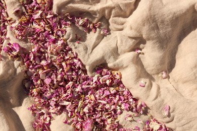 Scattered dried tea rose flowers and petals on beige fabric, top view