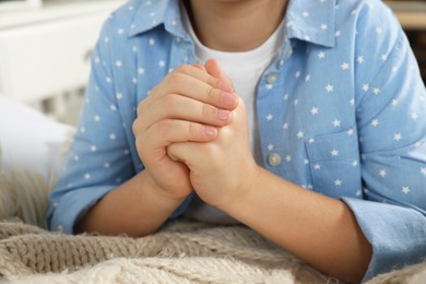 Photo of Girl with clasped hands praying near bed, closeup