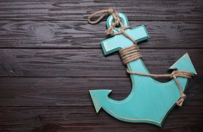 Photo of Anchor with hemp rope on dark wooden table, top view. Space for text