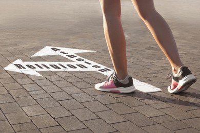 Choice between atheism and religion. Woman walking towards drawn marks on road, closeup. Arrows with words pointing in opposite directions