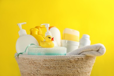 Photo of Basket with baby cosmetic products and accessories on yellow background