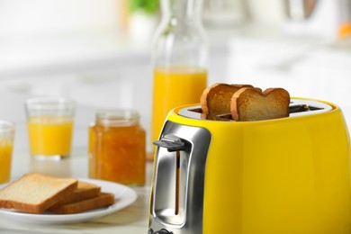 Yellow toaster with roasted bread slices on white table, closeup