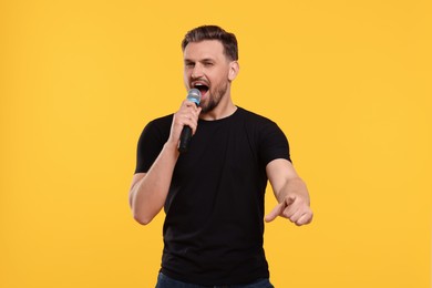Handsome man with microphone singing on yellow background