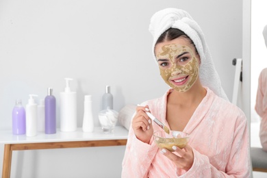 Photo of Young woman applying clay mask on her face in bathroom, space for text. Skin care