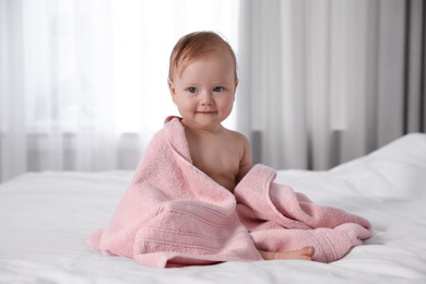 Photo of Cute little baby with soft pink towel on bed after bath