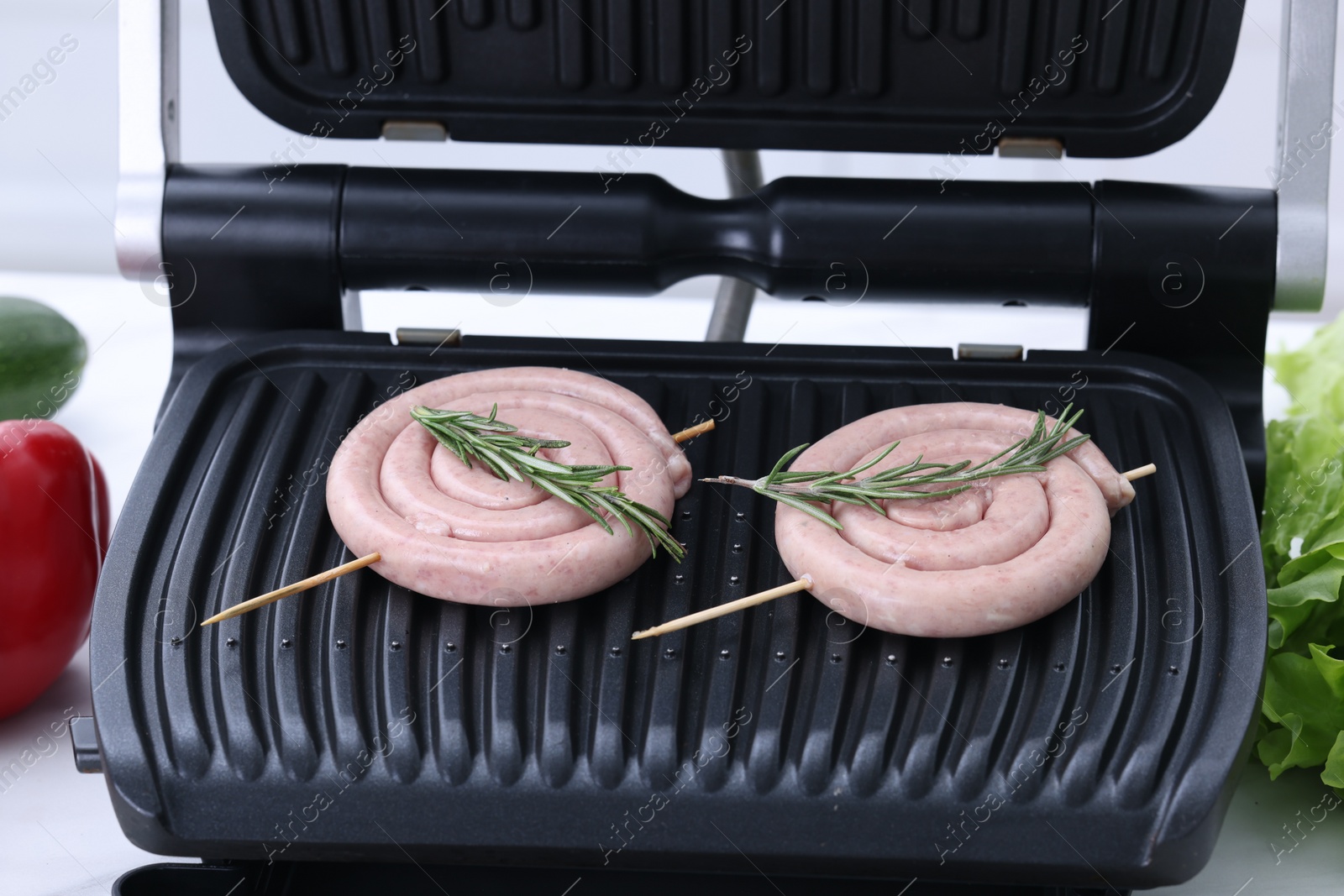 Photo of Electric grill with homemade sausages and rosemary on table, closeup