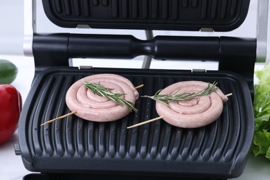 Electric grill with homemade sausages and rosemary on table, closeup