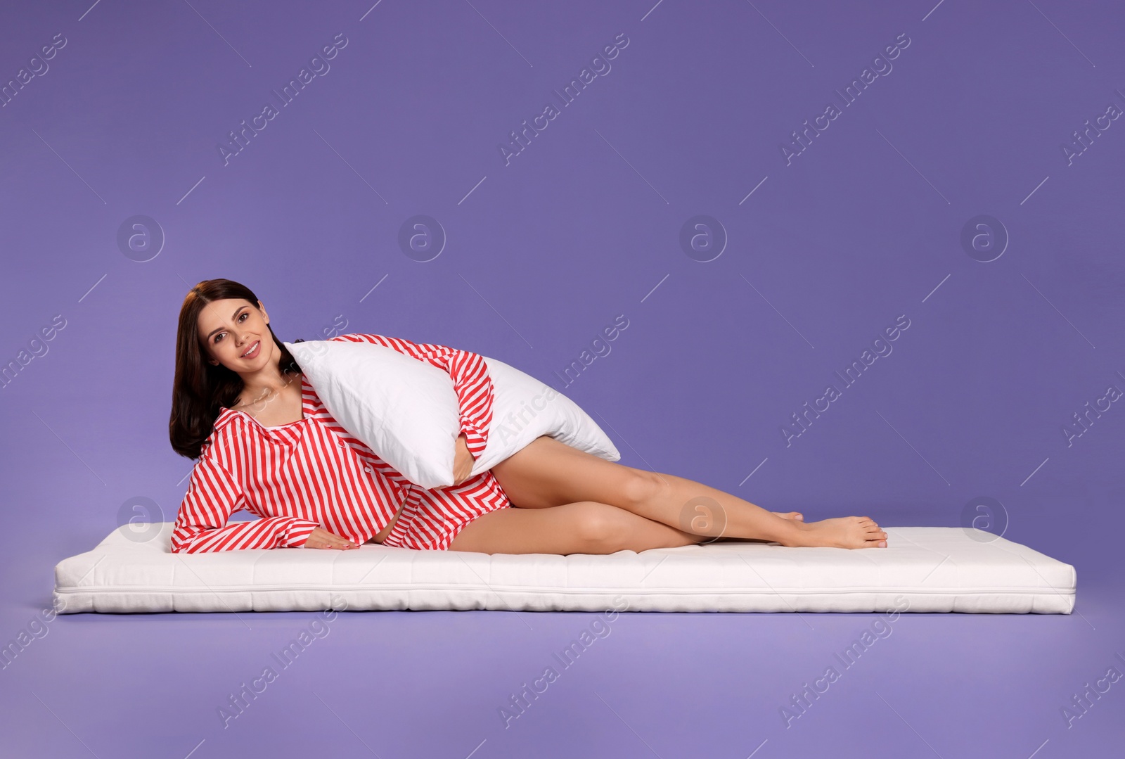 Photo of Young woman lying on soft mattress and holding pillow against light purple background