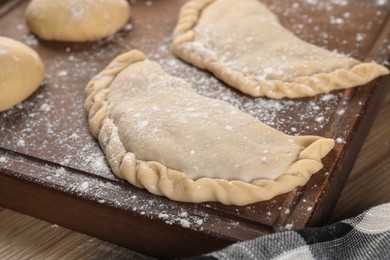 Photo of Raw chebureki with tasty filling on wooden table, closeup