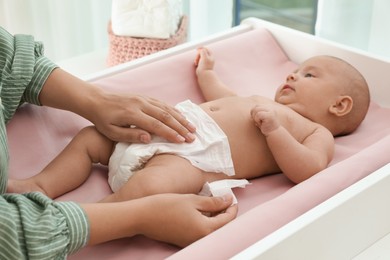 Mother changing her baby's diaper on table at home