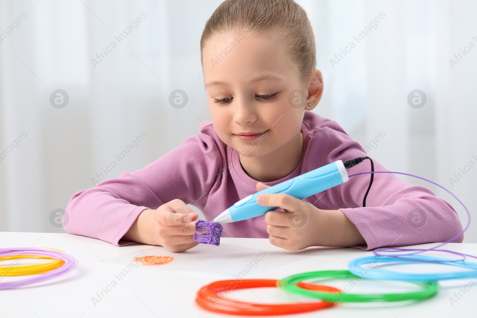 Photo of Girl drawing with stylish 3D pen at white table indoors