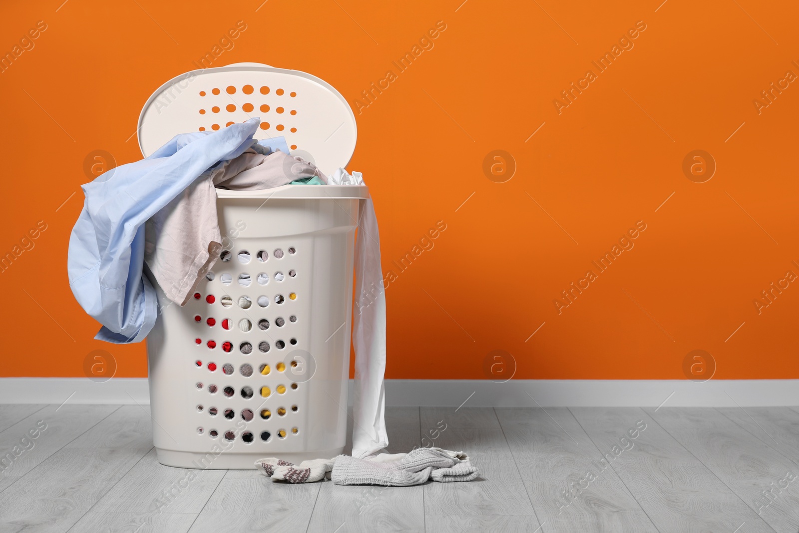 Photo of Laundry basket with clothes near orange wall. Space for text