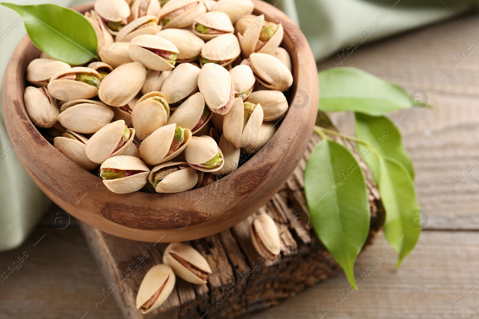 Photo of Delicious pistachios in bowl on wooden table, closeup